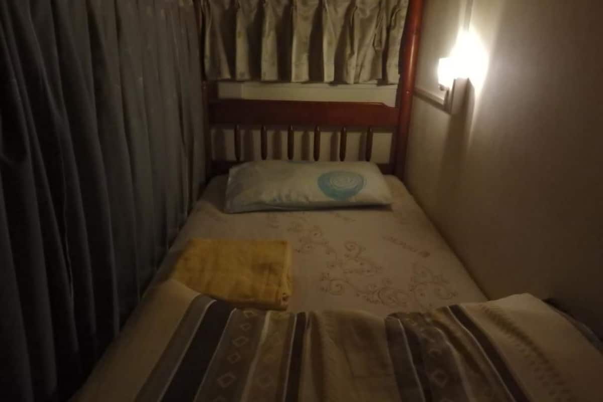 Ein kleiner, schwach beleuchteter Raum mit einem Bett, einem Kopfkissen und einer Decke.