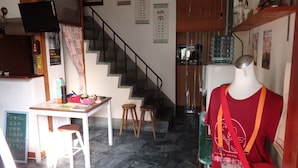 L’intérieur d’un restaurant avec un escalier, une table avec des tabourets, un mannequin tenant un sac, et divers panneaux accrochés aux murs.