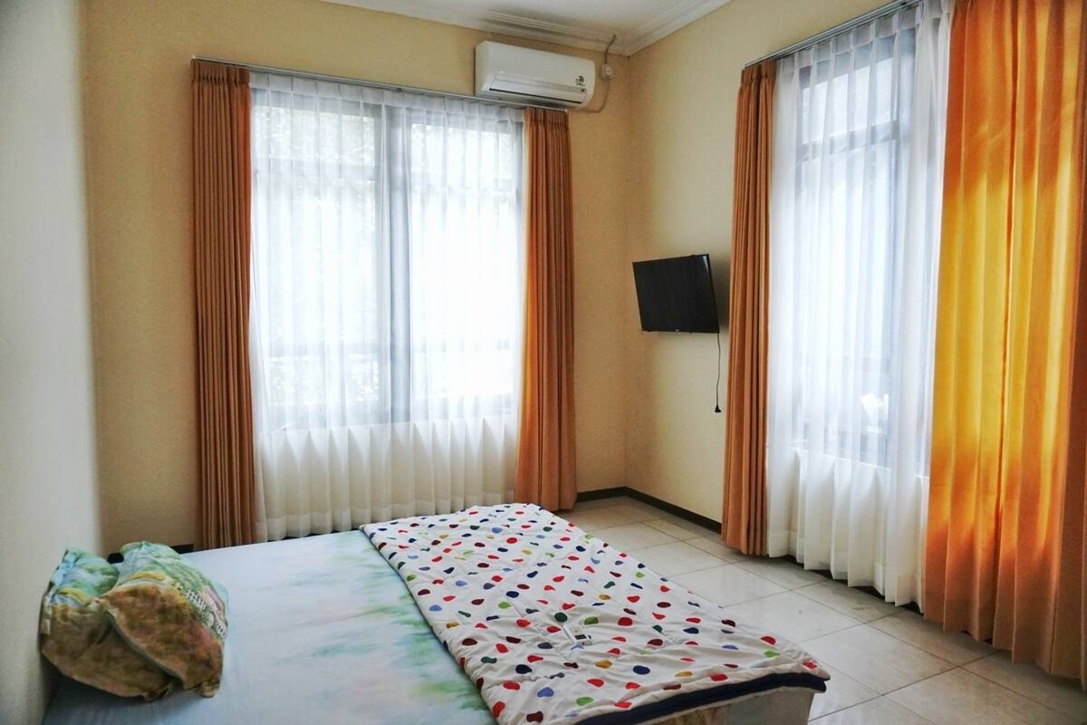 A hotel room with a bed, curtains, an air conditioning unit, and a flat-screen TV.