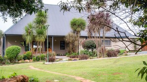 A house with a grey roof, surrounded by a well-maintained garden with various plants and a pathway leading to the entrance. - Mount Shekinah Country Hotel (Balgowan)