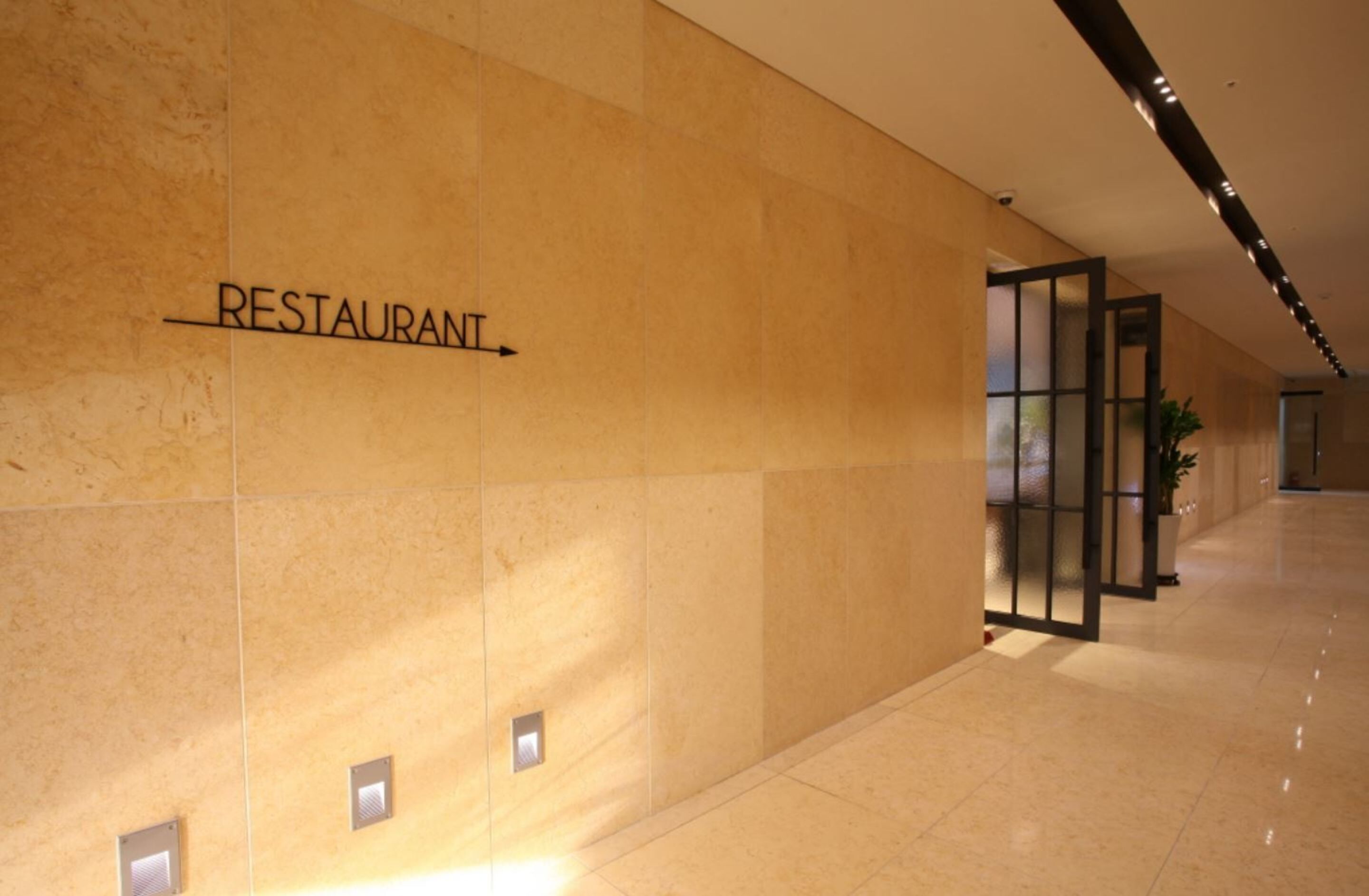 A hallway with a sign reading "RESTAURANT" on the wall, a potted plant, and a modern interior design.