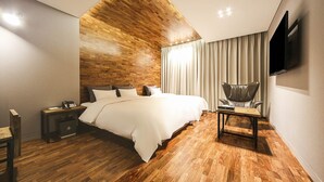 Una habitación de hotel moderna con techo de madera, una cama grande, un escritorio, una silla y un televisor montado en la pared.