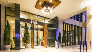 Una entrada de hotel moderna con puertas de vidrio, plantas en macetas y un diseño de techo de madera.