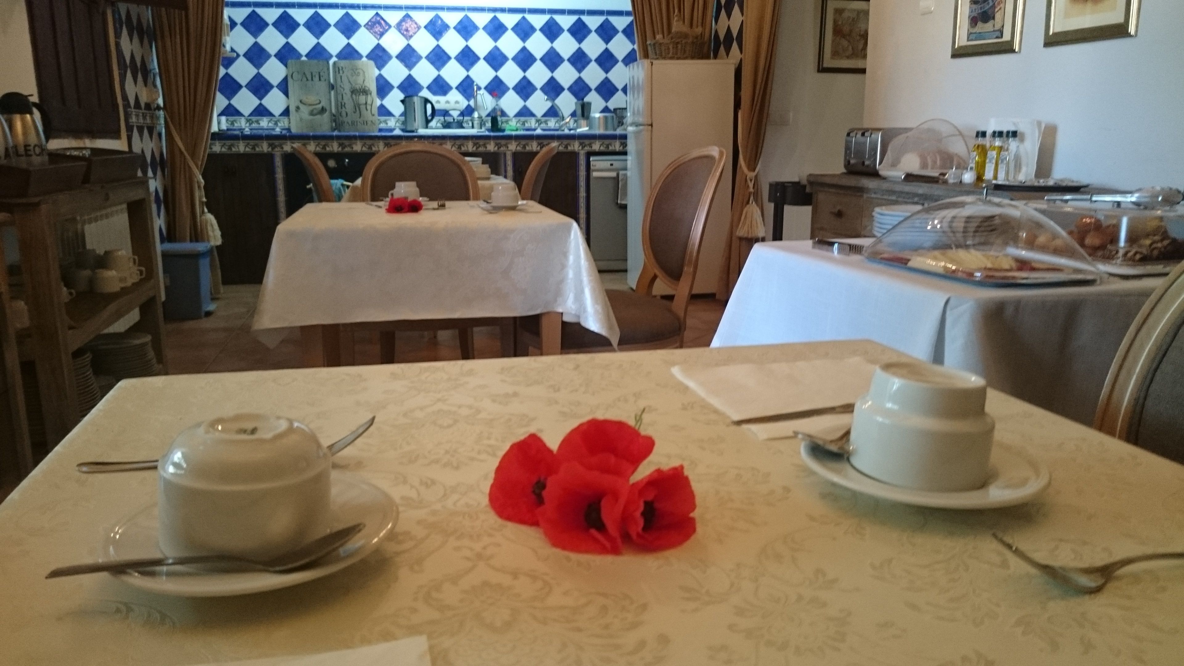 Un comedor con una mesa dispuesta para dos, una cocina al fondo y una mesa de comedor con mantel blanco.