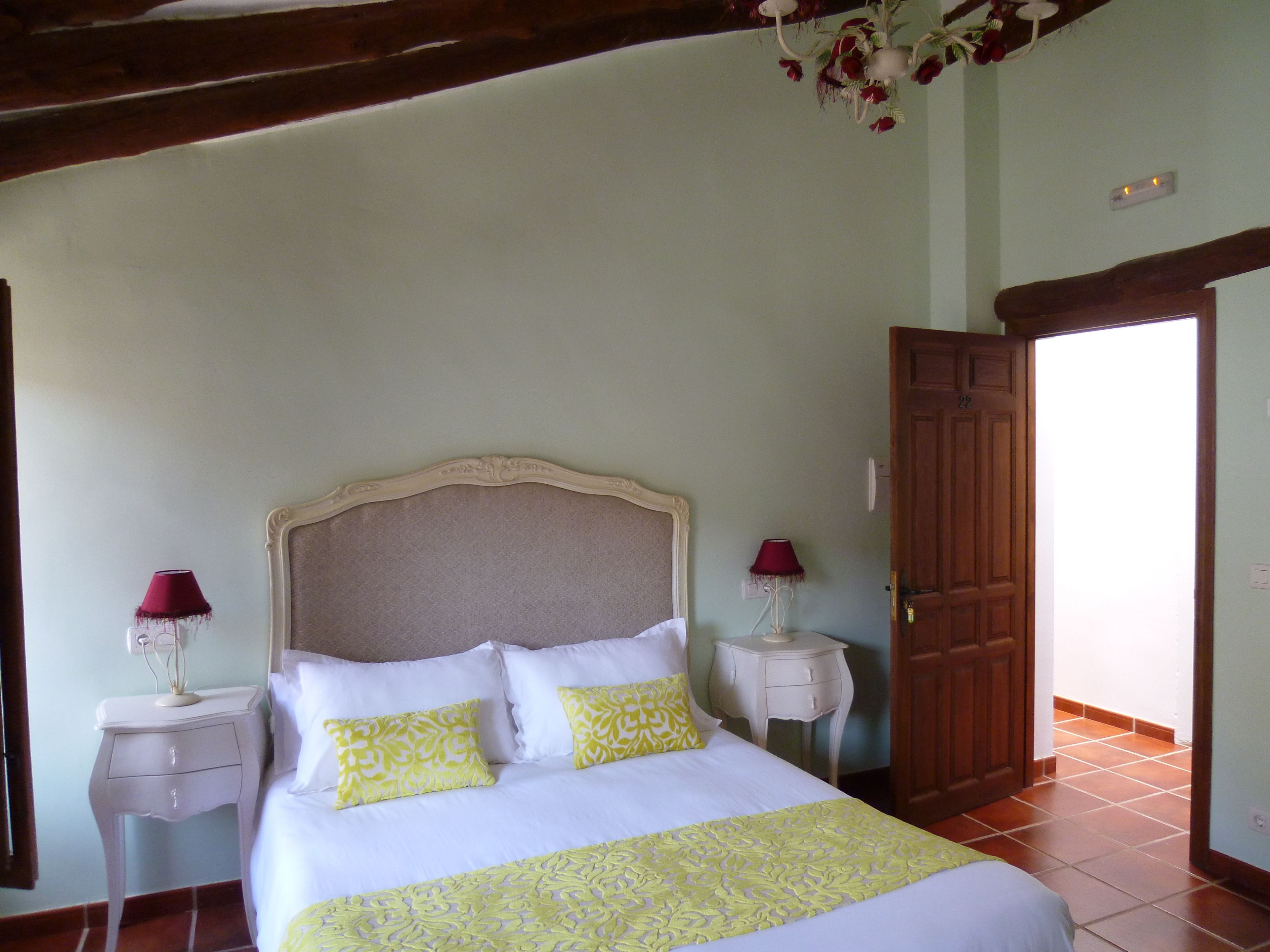 A bedroom with a bed, two bedside tables, a chandelier, and a wooden door.