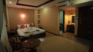 Hotelkamer met een groot bed, een bureau, een stoel, een tafeltje met een vaas en een airconditioning.