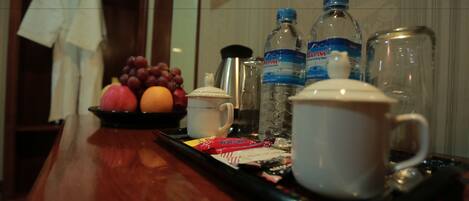 A tray with fruits, a white mug, and two water bottles on a wooden table in a hotel room.
