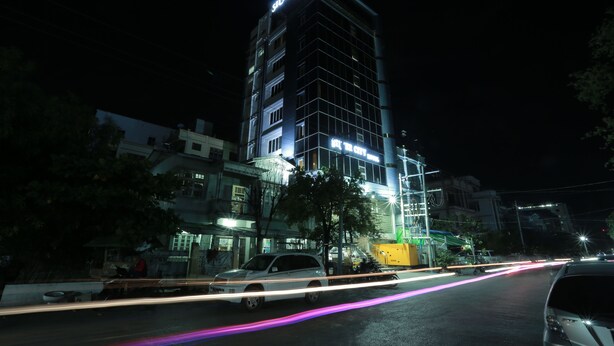 Een meerlaags hotel met verlichte signage, een modern architectonisch ontwerp en een straatbeeld met passerend verkeer.