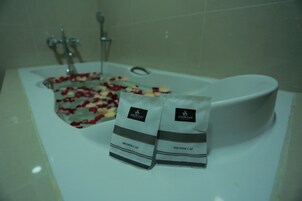 Un baño con una bañera llena de pétalos de rosa y dos gorros de ducha con la etiqueta 'Silver City Hotel'.