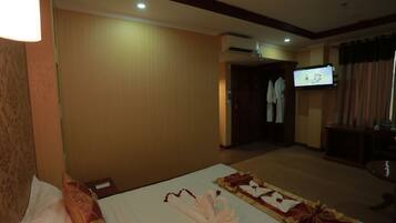 Habitación de hotel con una cama bien hecha, un televisor en la pared y un perchero al fondo.