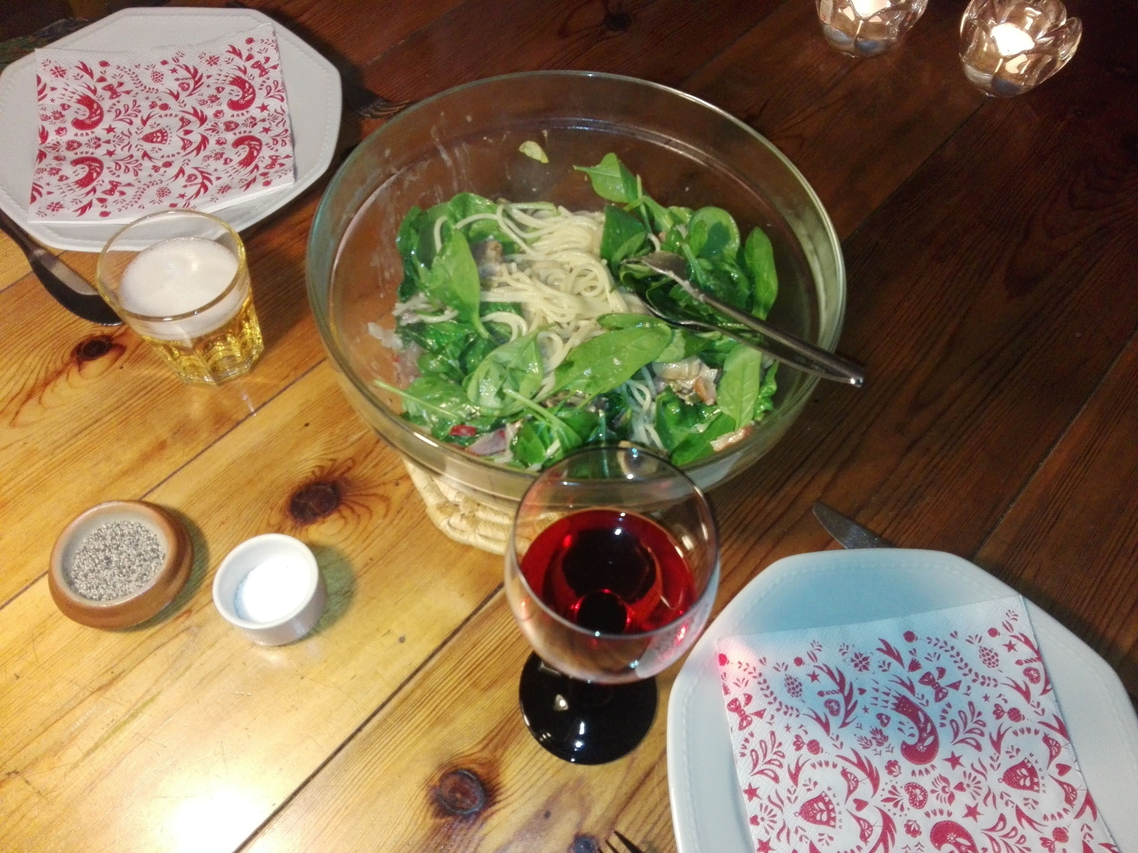 A table with a glass bowl of salad, a glass of red wine, and a plate with a patterned napkin.