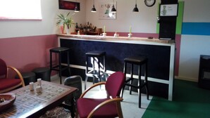 Een knusse bar met houten balken, een toonbank met krukken en een klok aan de muur.