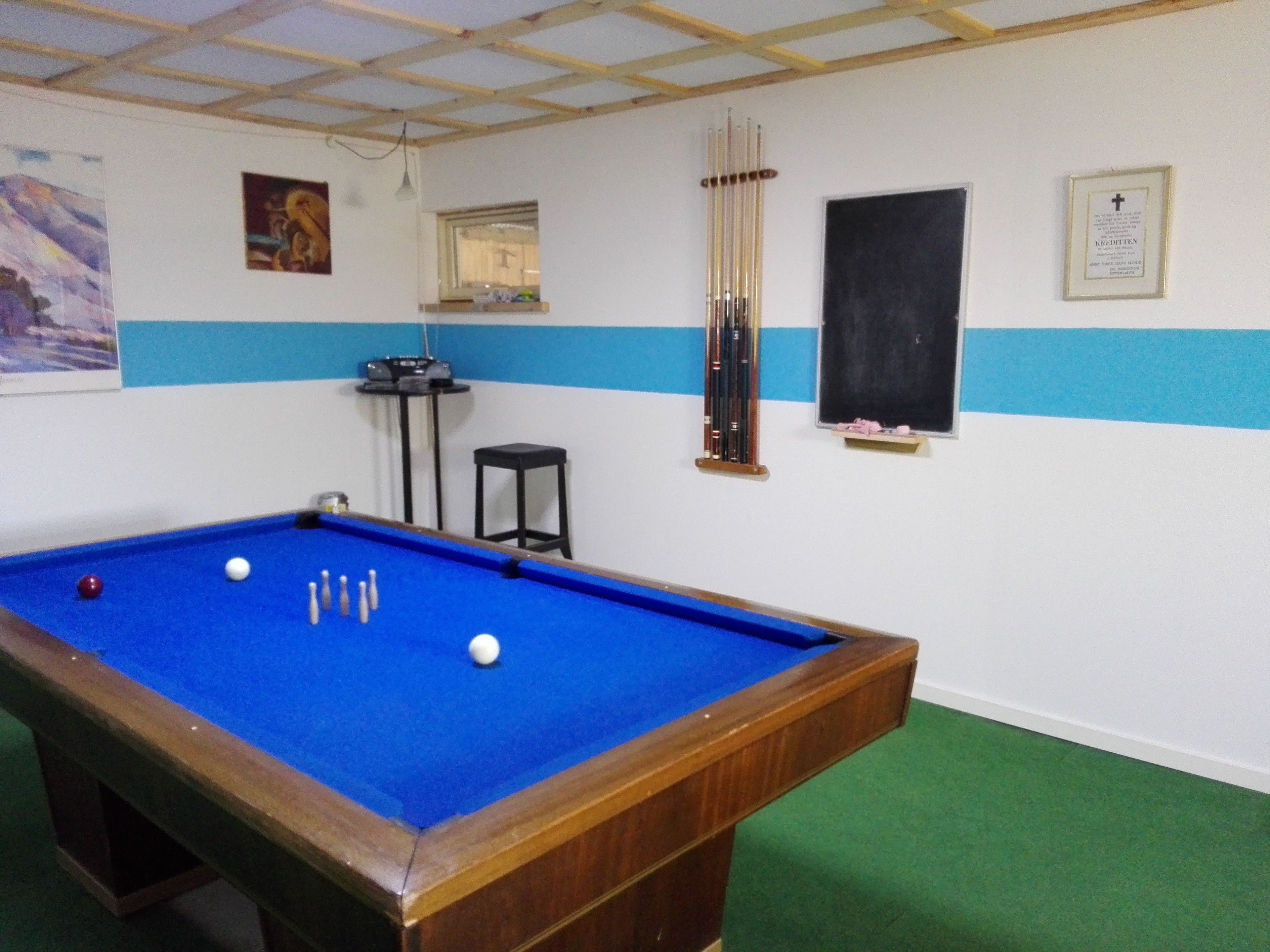 A pool table with balls, a cue rack, and a framed certificate on the wall.