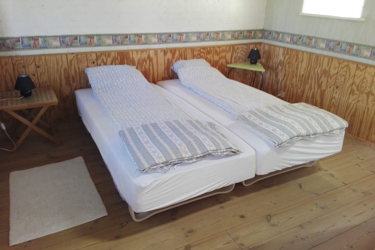 Quarto com duas camas, uma mesa pequena, um abajur e uma janela.