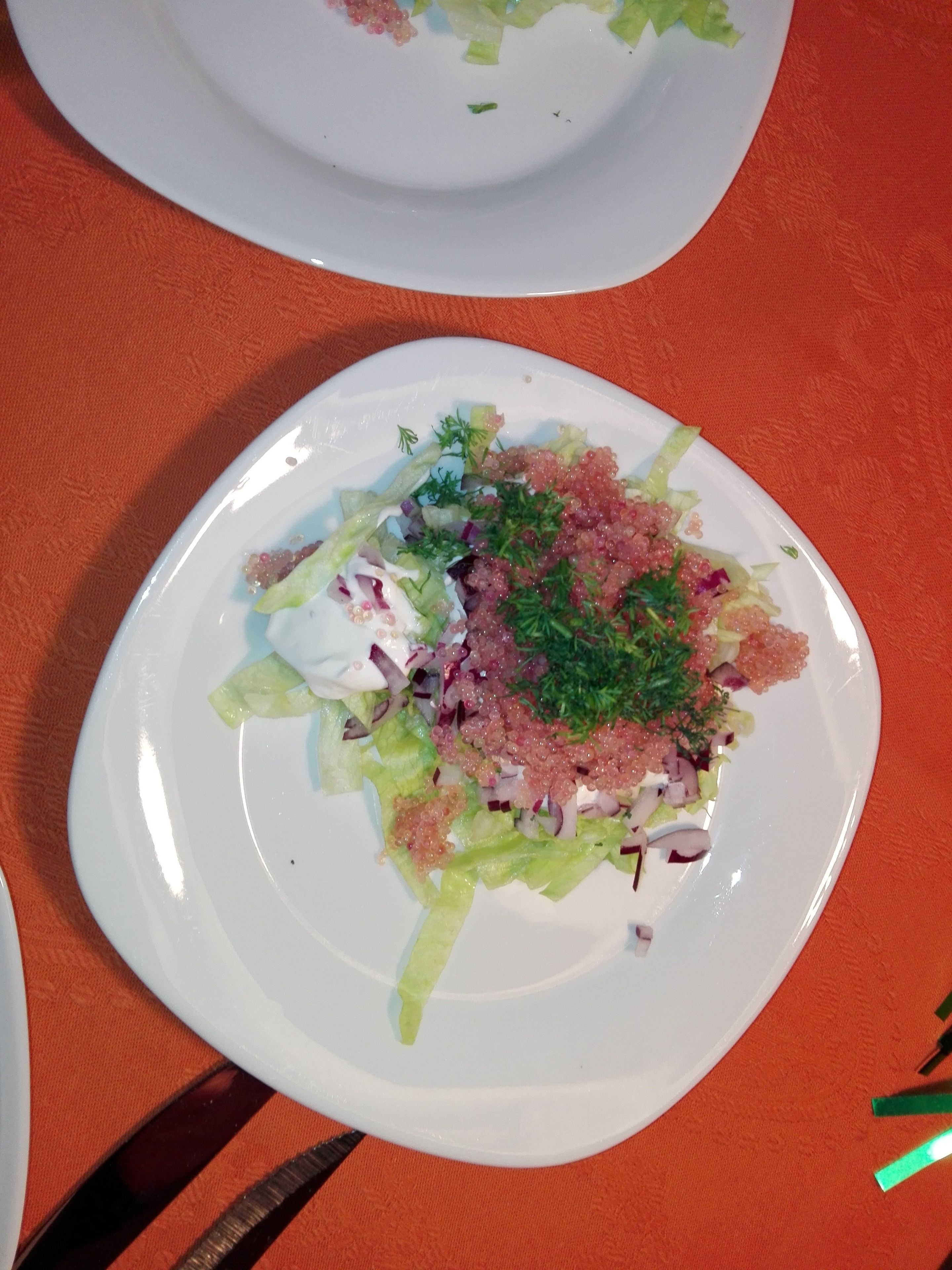 Une assiette blanche avec une salade, posée sur une nappe orange.