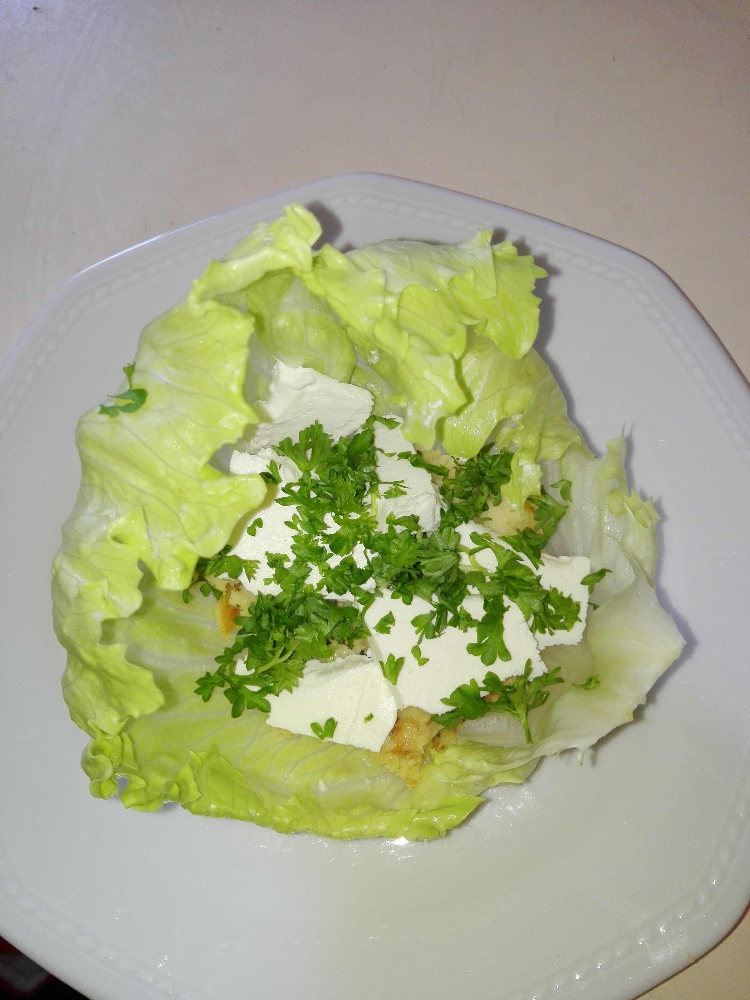 A plate with a salad consisting of lettuce, a white creamy topping, and parsley.
