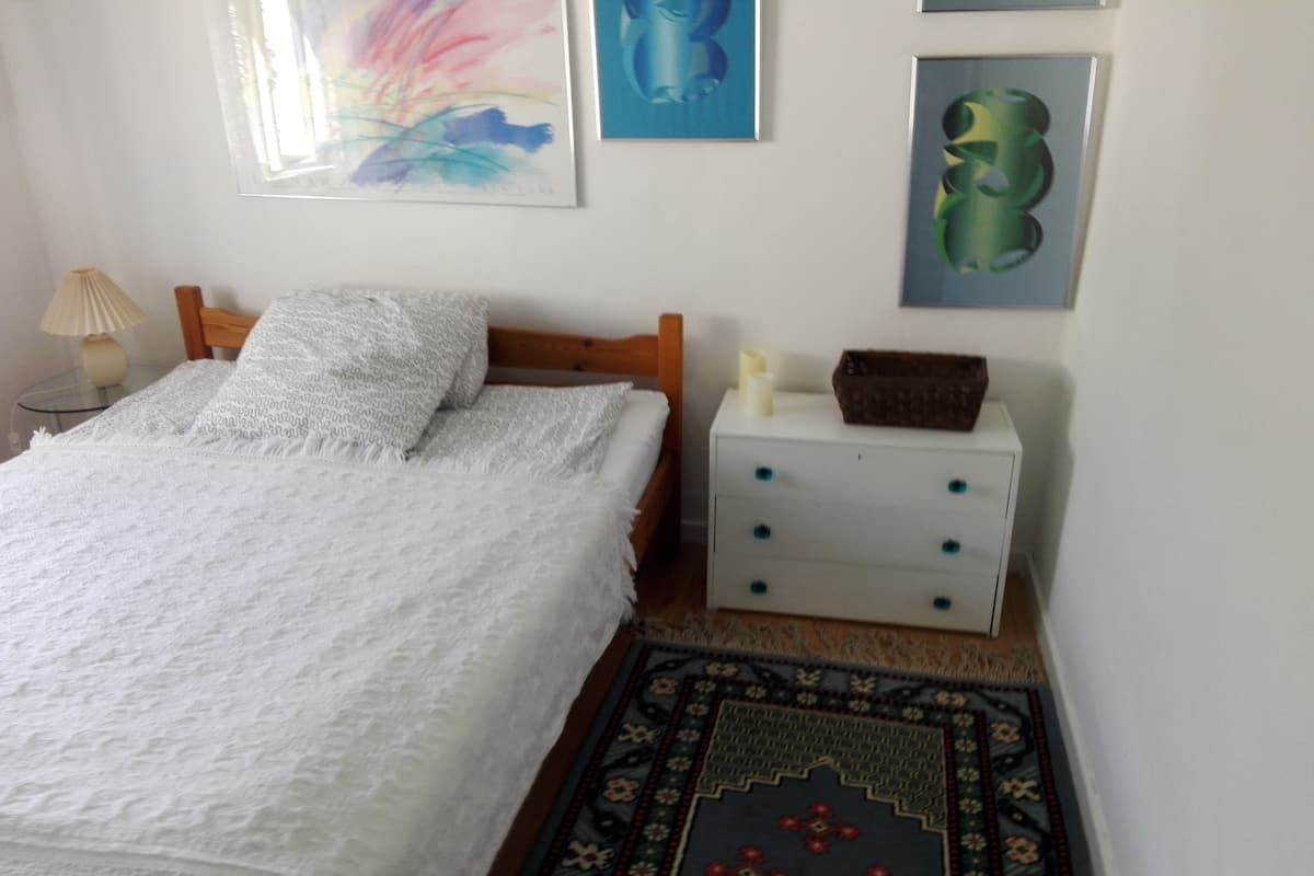 Quarto com cama, mesa de cabeceira e quadros na parede.