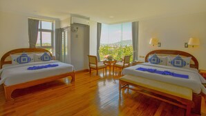 Habitación de hotel con dos camas, una mesita, sillas y vistas a la ciudad.