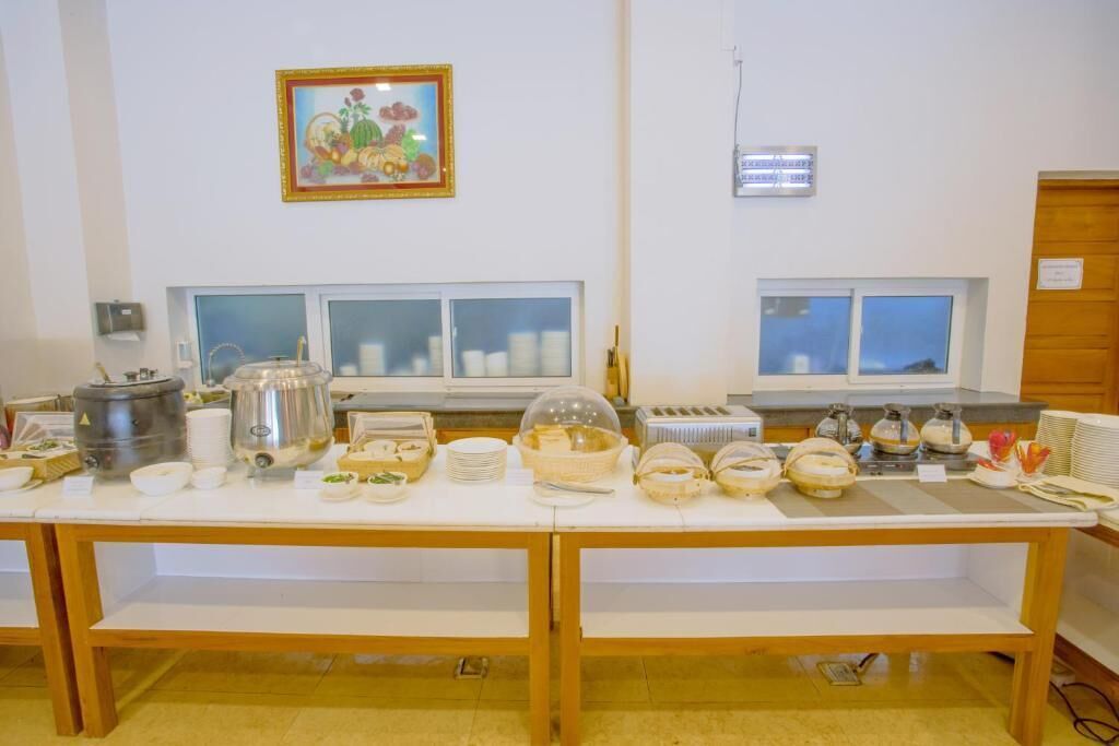 A buffet setup with various food items and serving utensils on a long table, with windows in the background.