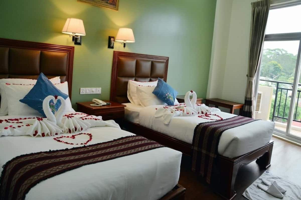 A hotel room with two beds, each adorned with a heart-shaped flower arrangement and swan decorations.