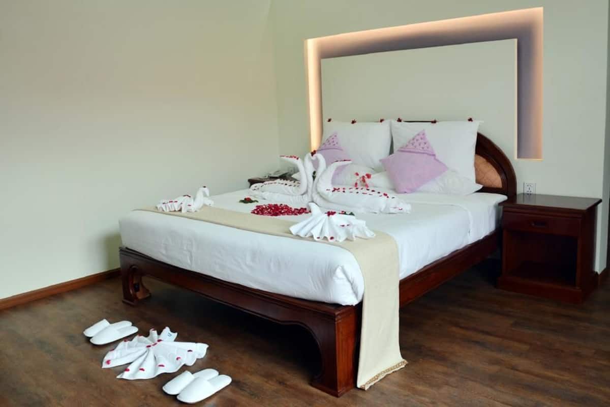 A neatly made bed with white linens, a wooden headboard, and a bedside table.