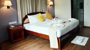 Une chambre d’hôtel avec un lit en bois, deux lampes de chevet, un téléphone et une porte en verre donnant sur une salle de bain.