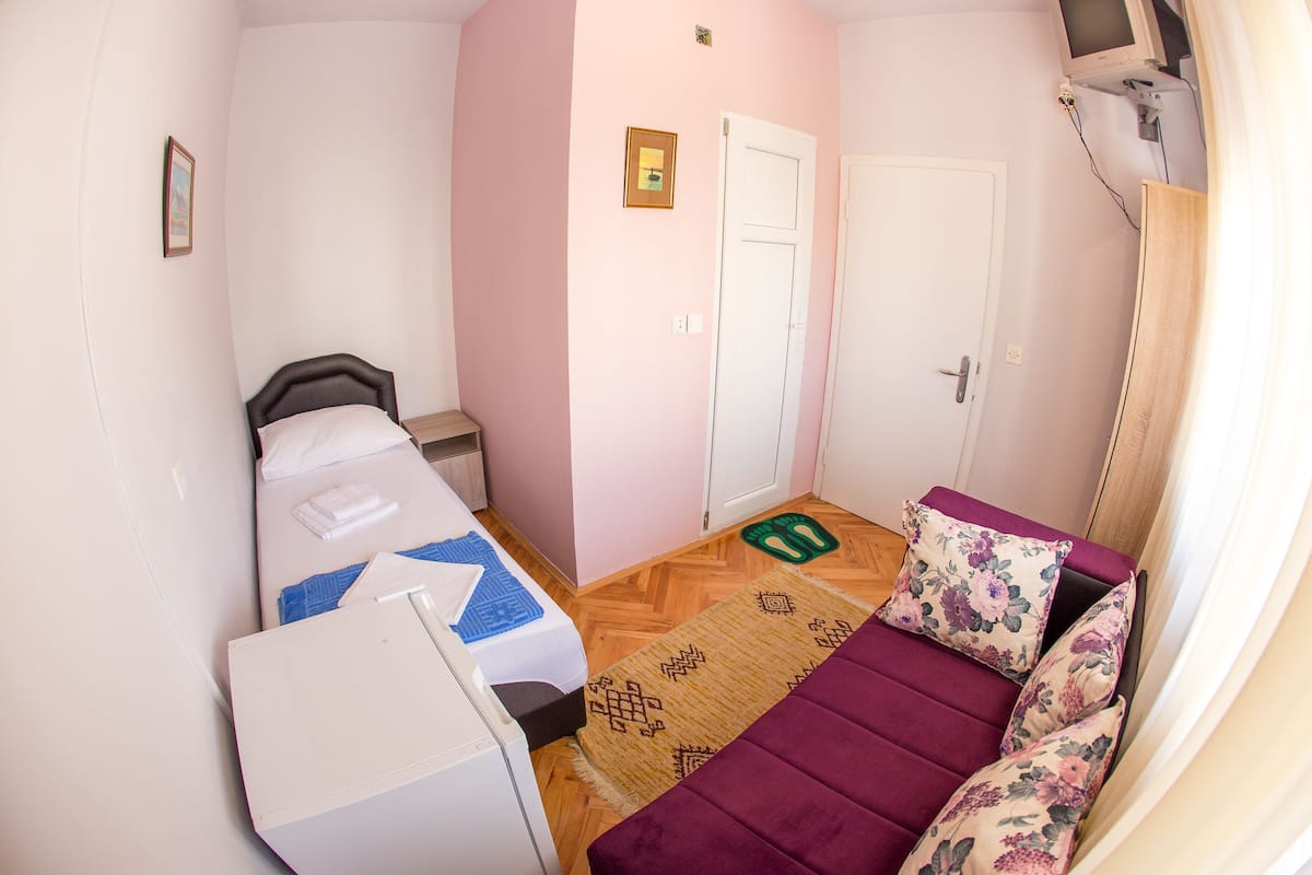 Una habitación pequeña con cama, sofá, escritorio y puerta.