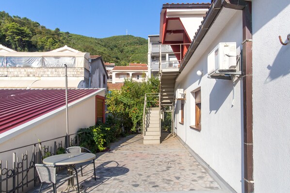A narrow alleyway with a tiled floor, a small table and chairs, and a staircase leading to a balcony.