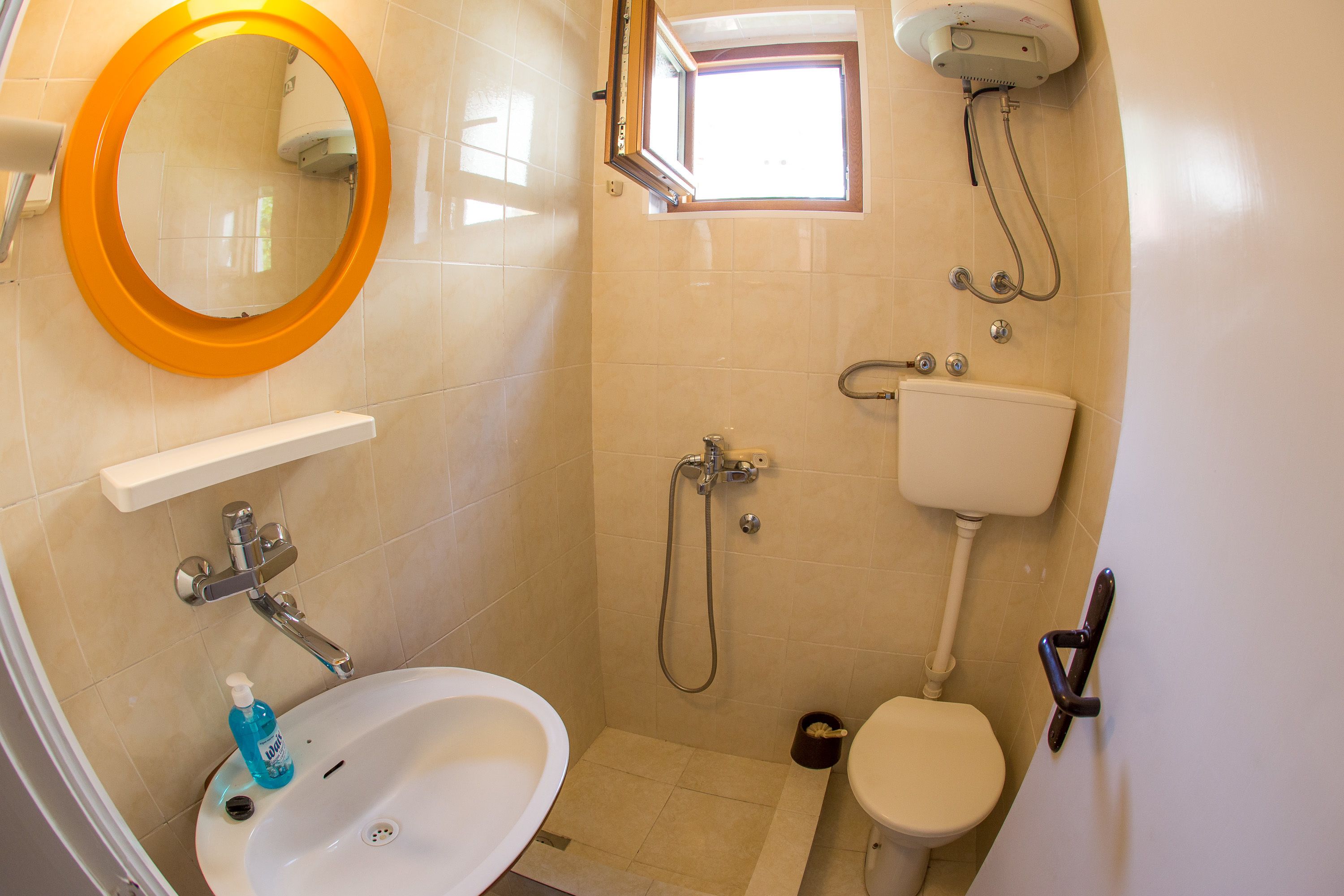 A bathroom with a white sink, a mirror with an orange frame, a toilet, and a shower with a handheld showerhead.