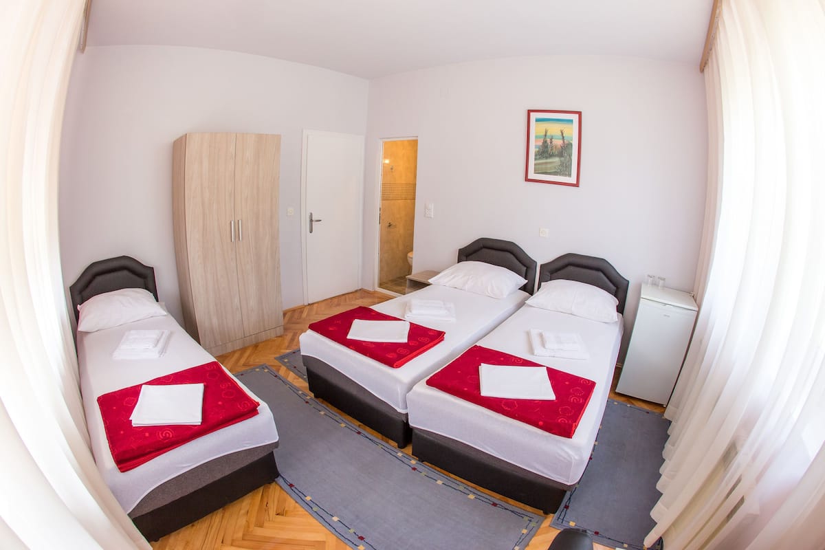 Habitación de hotel con tres camas, un armario, un refrigerador pequeño y un cuadro en la pared.