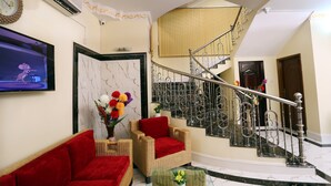 A living room with a red sofa, wicker armchairs, a marble fireplace, and a staircase with metal railings. - Hotel-All Season Lodge (Sylhet)