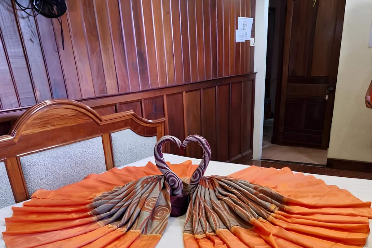 Una cama con sábana blanca y un arreglo decorativo de tela naranja en la colcha, que recuerda a un cisne.