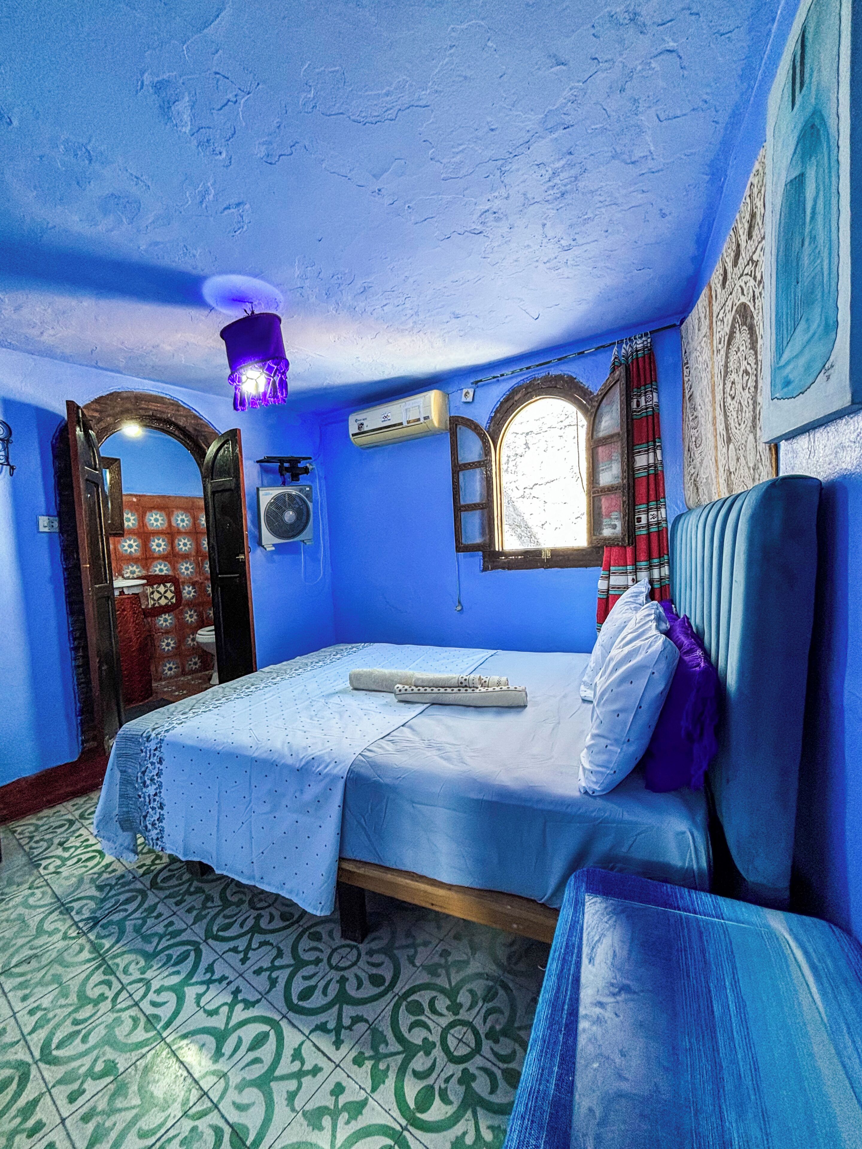 Een kamer met een bed, een raam met gordijnen, een wandairconditioner en vloertegels met een patroon.
