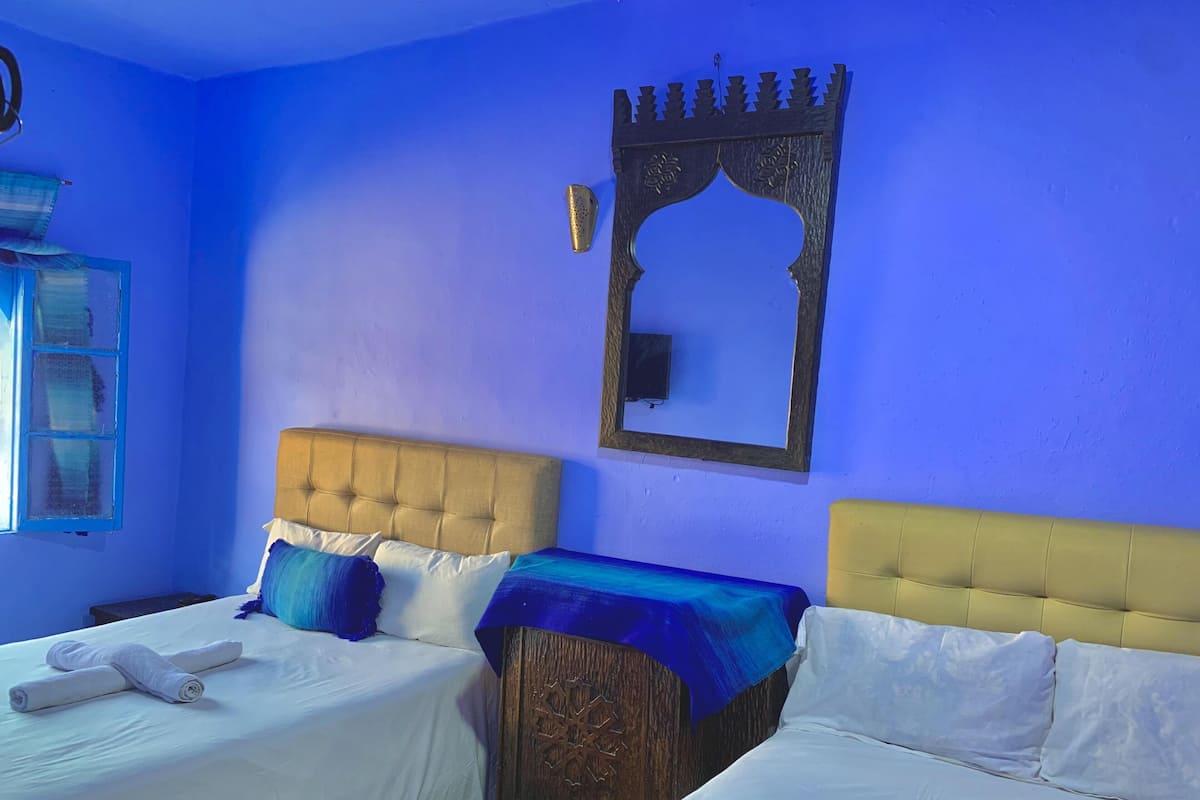 A room with two beds, a wooden headboard, a mirror, and a blue wall.