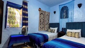 A room with two beds, a window with curtains, a patterned floor, and a hanging light fixture.