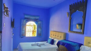 Habitación con dos camas, una ventana con reja decorativa, un espejo y una pared azul.