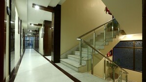 Un pasillo de hotel moderno con una escalera de cristal y vistas al vestíbulo.