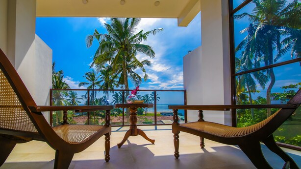 A balcony with two wicker chairs and a small table, overlooking a beach with palm trees and a clear sky. - Sath Villa Naadi Ayurveda Resort (Beruwala)