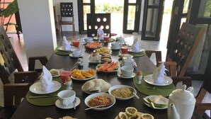 A breakfast buffet with various dishes, including toast, fruit, and beverages, set on a wooden table with chairs. - Sath Villa Naadi Ayurveda Resort (Beruwala)