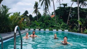 A swimming pool with three people in the water, surrounded by lush greenery and palm trees. - Sath Villa Naadi Ayurveda Resort (Beruwala)