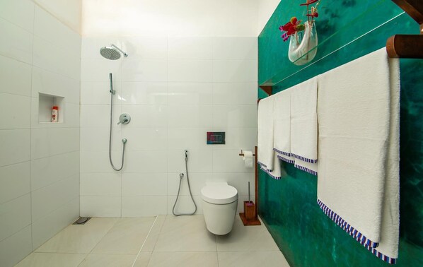 Un baño con azulejos blancos, ducha, inodoro y toallero con toallas.