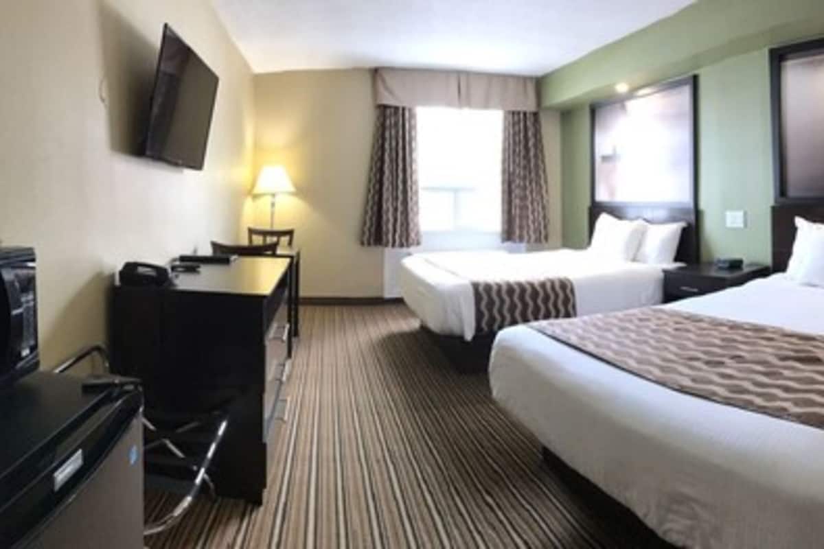 Quarto de hotel com duas camas, uma escrivaninha com abajur, televisão e uma janela grande com cortinas.