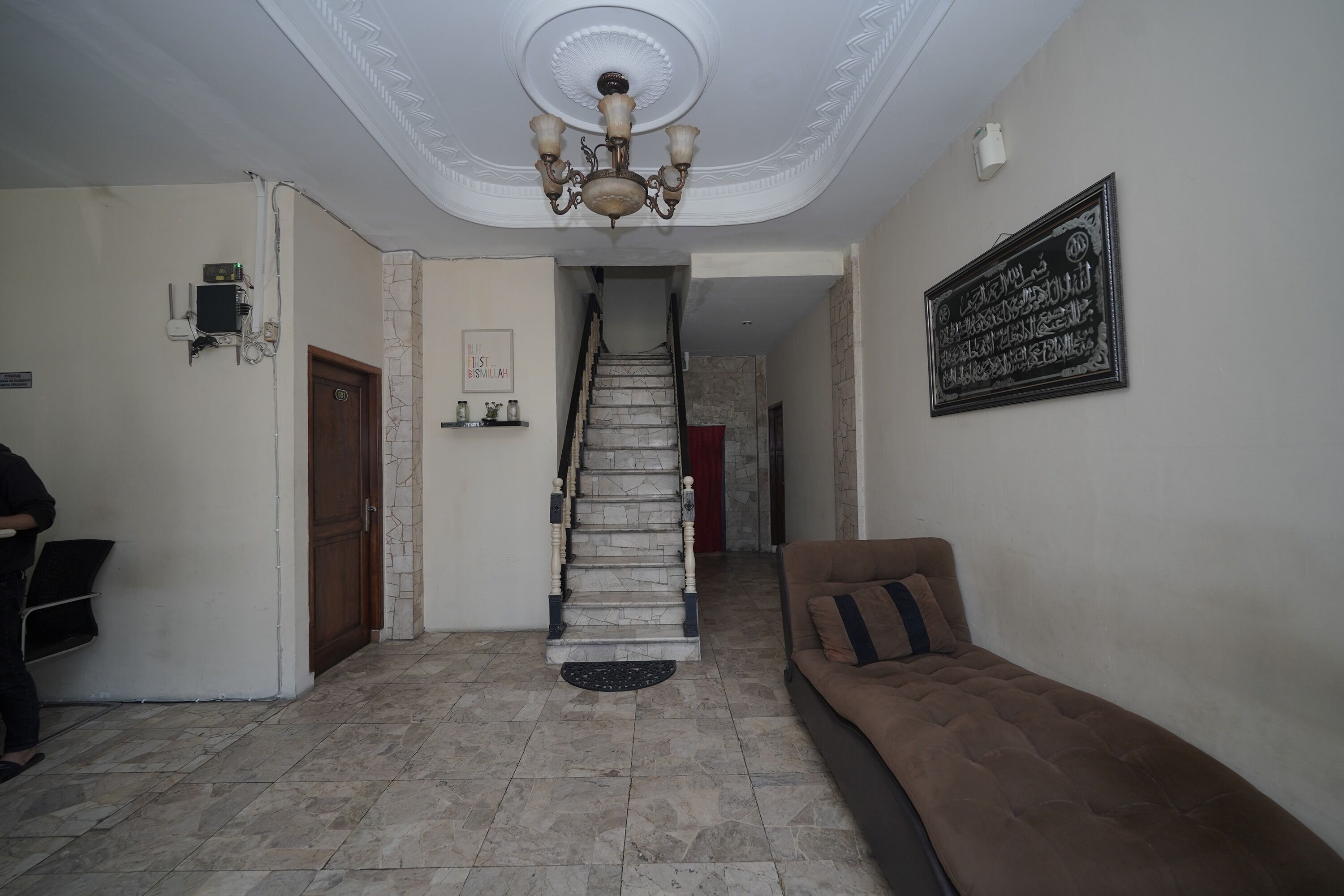 A hallway with a staircase, a brown sofa, and a chandelier.