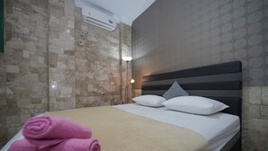 A hotel room with a bed, a wall-mounted air conditioner, and a patterned wall.