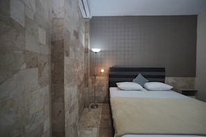 A hotel room with a stone wall, a bed with white bedding, a headboard, and a floor lamp. - Wisma Asia Busindo Syariah (Bandung)