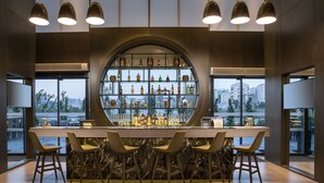 A modern bar with a circular display of bottles, bar stools, and large windows offering city views. - Centro Westside by Rotana (Istanbul)