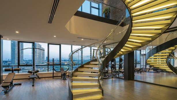 A modern gym with a spiral staircase, large windows, and a city view. - Centro Westside by Rotana (Istanbul)
