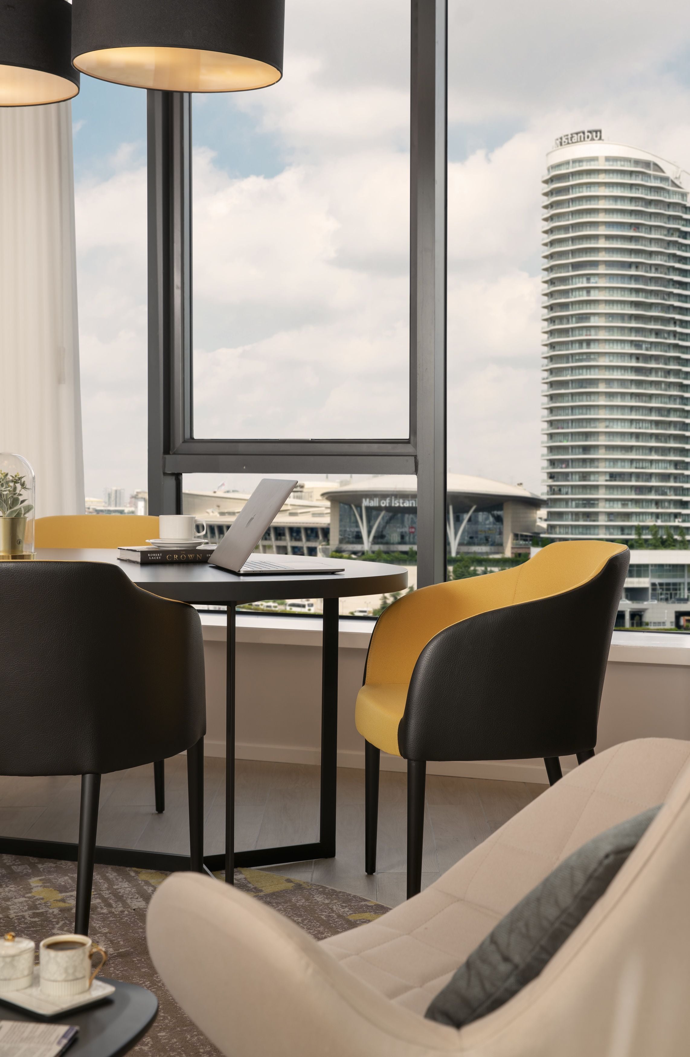 A modern hotel room with a large window, a laptop on a small table, and a view of a tall building labeled "Istanbul."