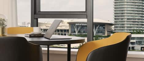 A modern hotel room with a large window, a laptop on a small table, and a view of a tall building labeled "Istanbul."
