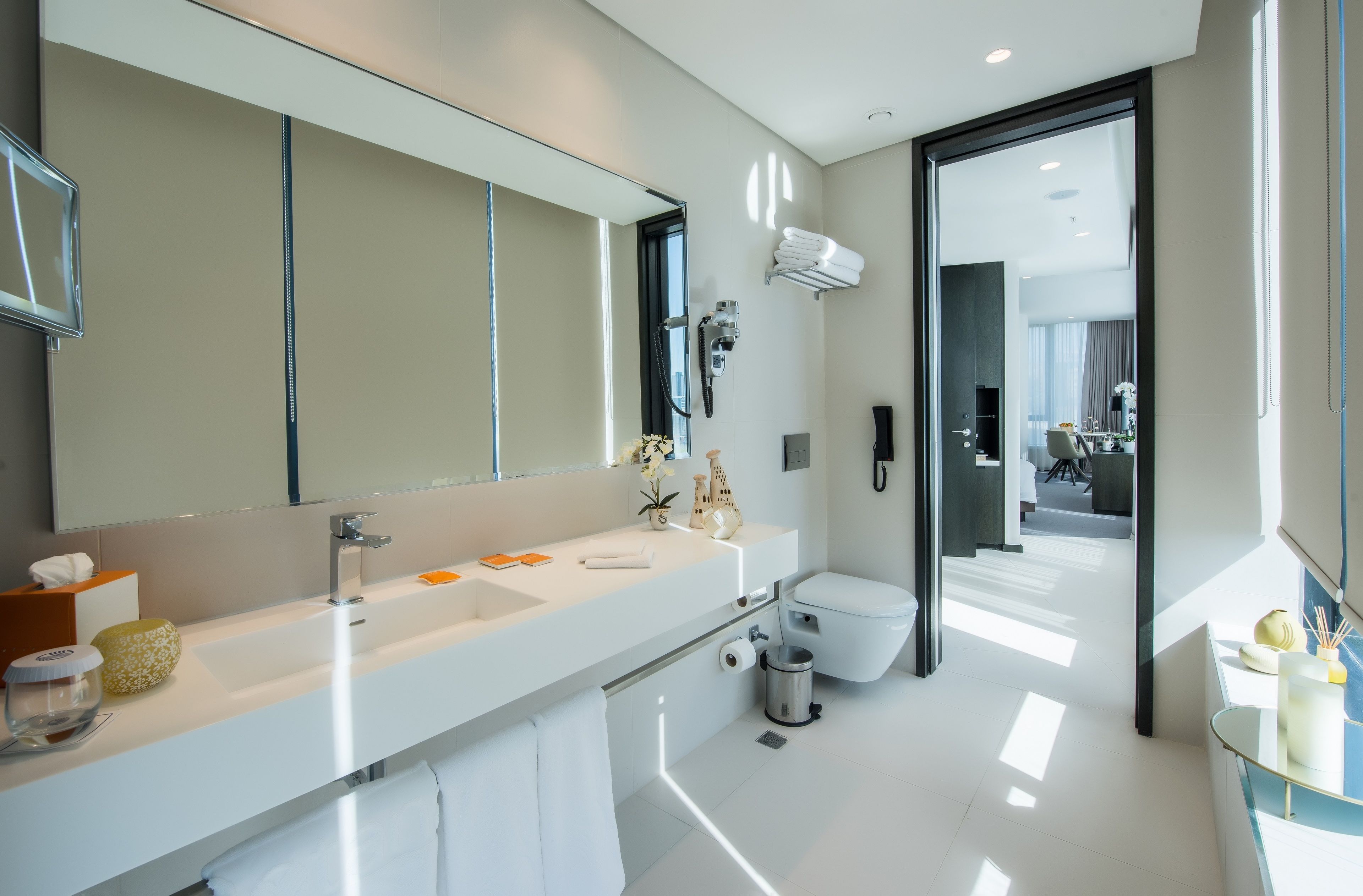 A modern bathroom with a large mirror, white sink, and a toilet.